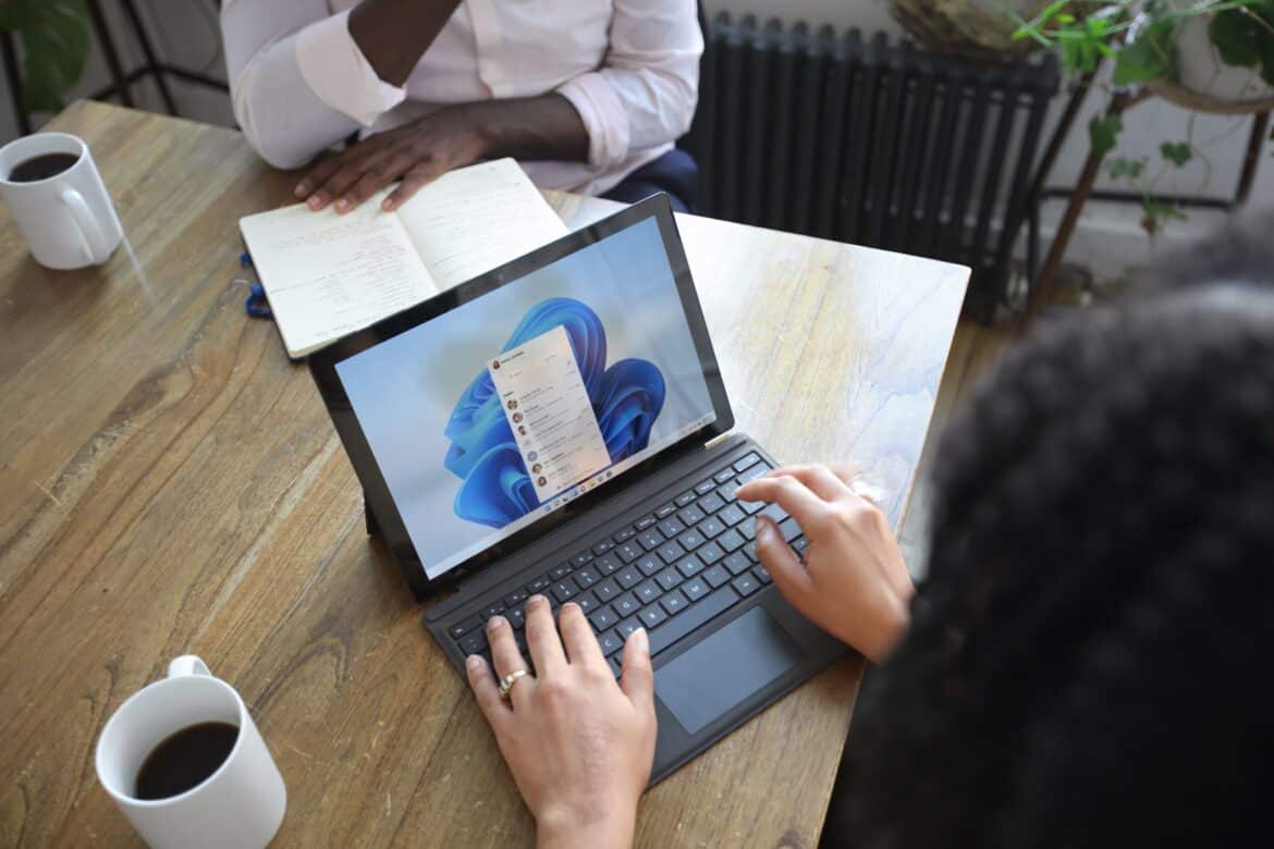 Overhead view of two people at a table working with a Microsoft laptop and notebook